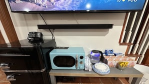 A kitchen area with a black refrigerator, a blue microwave, a coffee maker, and a small table with cereal boxes and a glass.
