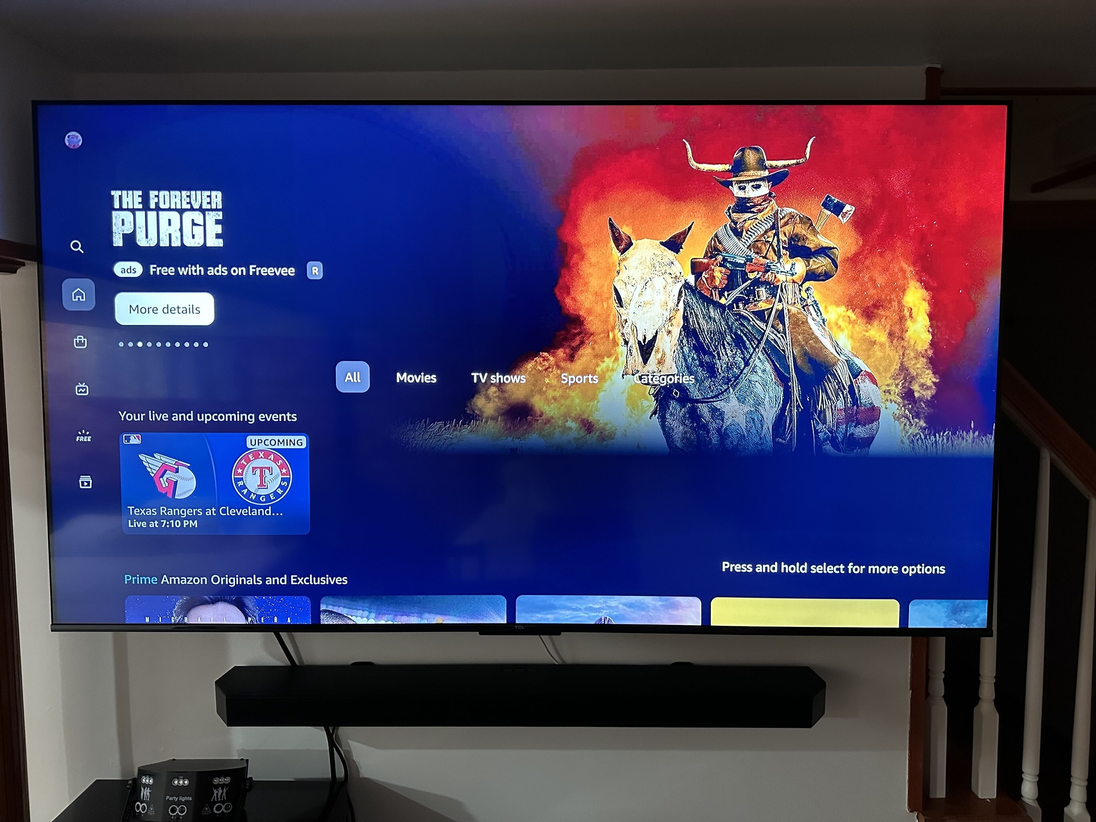 A television screen displaying a streaming service interface with a movie titled "The Forever Purge" and a sports event between Texas Rangers and Cleveland.