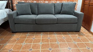 A grey sofa against a brick wall, a bed with white bedding, and a tiled floor with a geometric pattern.