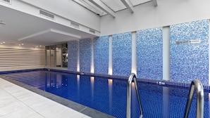 An indoor swimming pool with blue mosaic tiles, a no diving/no bombing sign, and a modern interior design.