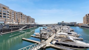 A marina with multiple boats docked, a building with balconies, and a clear sky.