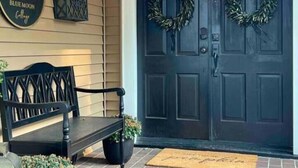 A front porch with a dark wooden door, two wreaths, a bench, and a lantern. - Blue Moon Cottage: Historic Owensboro Home w/ Large Pool, Music Room, Location! (Owensboro)