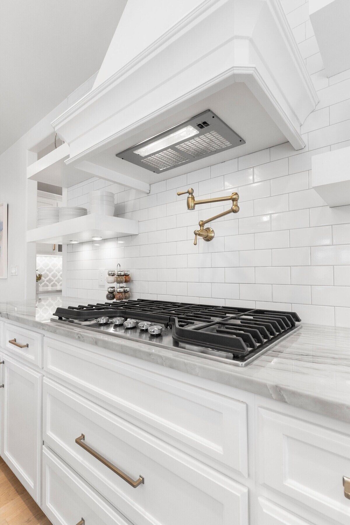 Una cocina moderna con armarios blancos, estufa a gas y campana extractora de acero inoxidable.