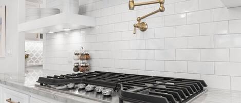 Una cocina moderna con armarios blancos, estufa a gas y campana extractora de acero inoxidable.