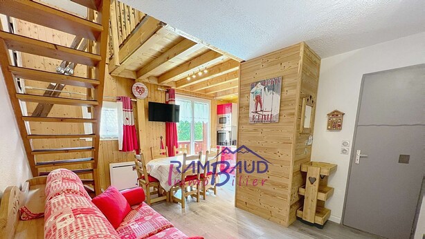Une pièce chaleureuse avec un plafond en bois, un coin repas comprenant une table et des chaises, et un canapé rouge agrémenté de coussins à motifs.