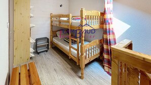 Une chambre avec un lit superposé, un plancher en bois, une fenêtre avec un rideau et une petite table.