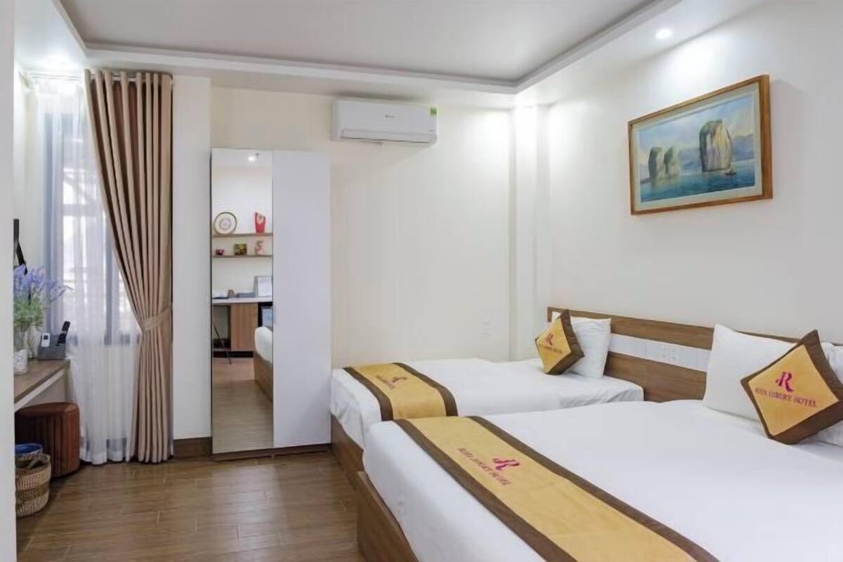 A hotel room with two beds, a painting on the wall, and an air conditioning unit.