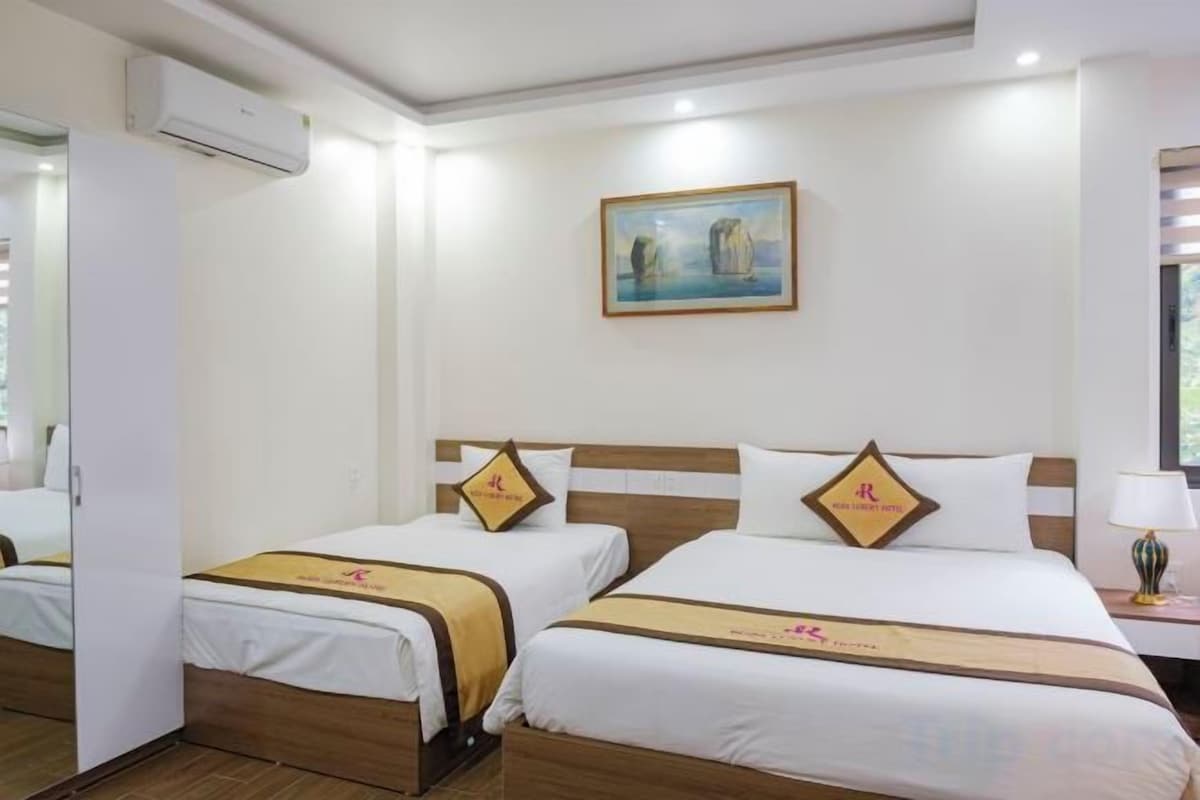 A hotel room with two beds, a painting on the wall, and a nightstand with a lamp.
