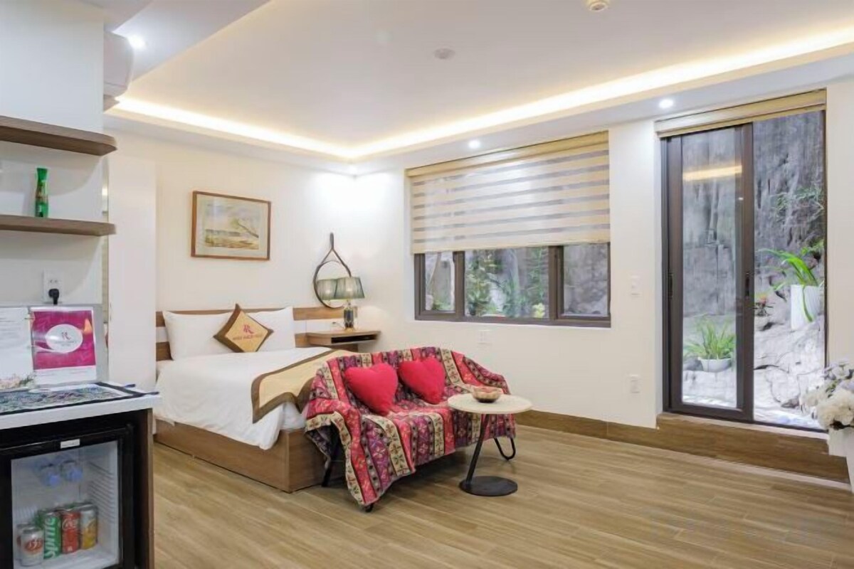 A modern bedroom with a bed, a sofa, a small table, and a sliding glass door leading to a balcony.
