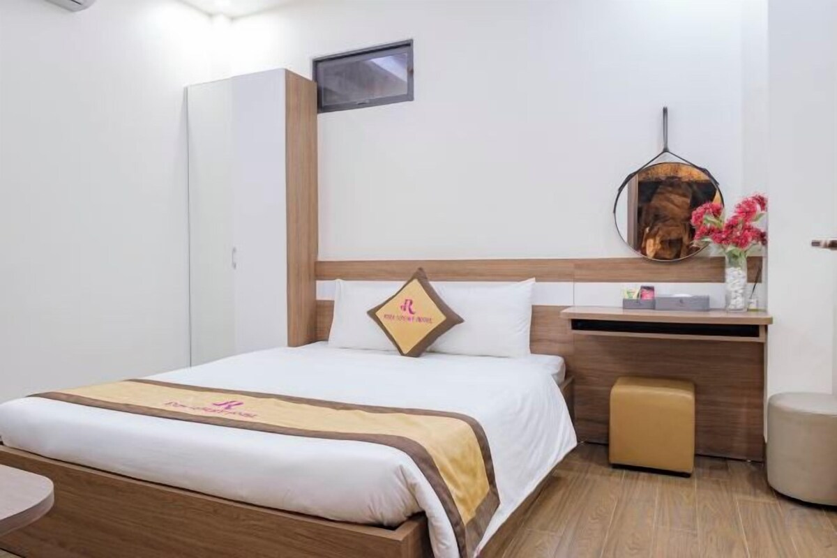 A hotel room with a bed, a desk, a chair, a wardrobe, and a mirror.