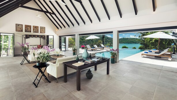 Amplia sala de estar con piscina, mobiliario exterior y vista a un paisaje tropical.