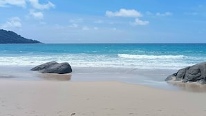Una playa con agua azul cristalina, orilla de arena y grandes rocas.