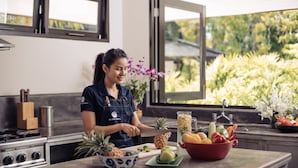 Una cocina con una persona preparando alimentos, una estufa, un lavamanos y diversas frutas y verduras sobre la encimera.
