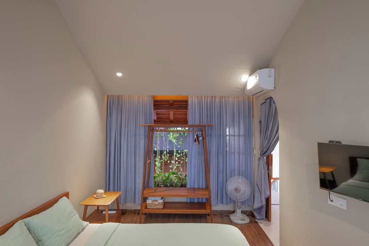 A bedroom with a bed, a small table with a cup, a fan, and a TV mounted on the wall.