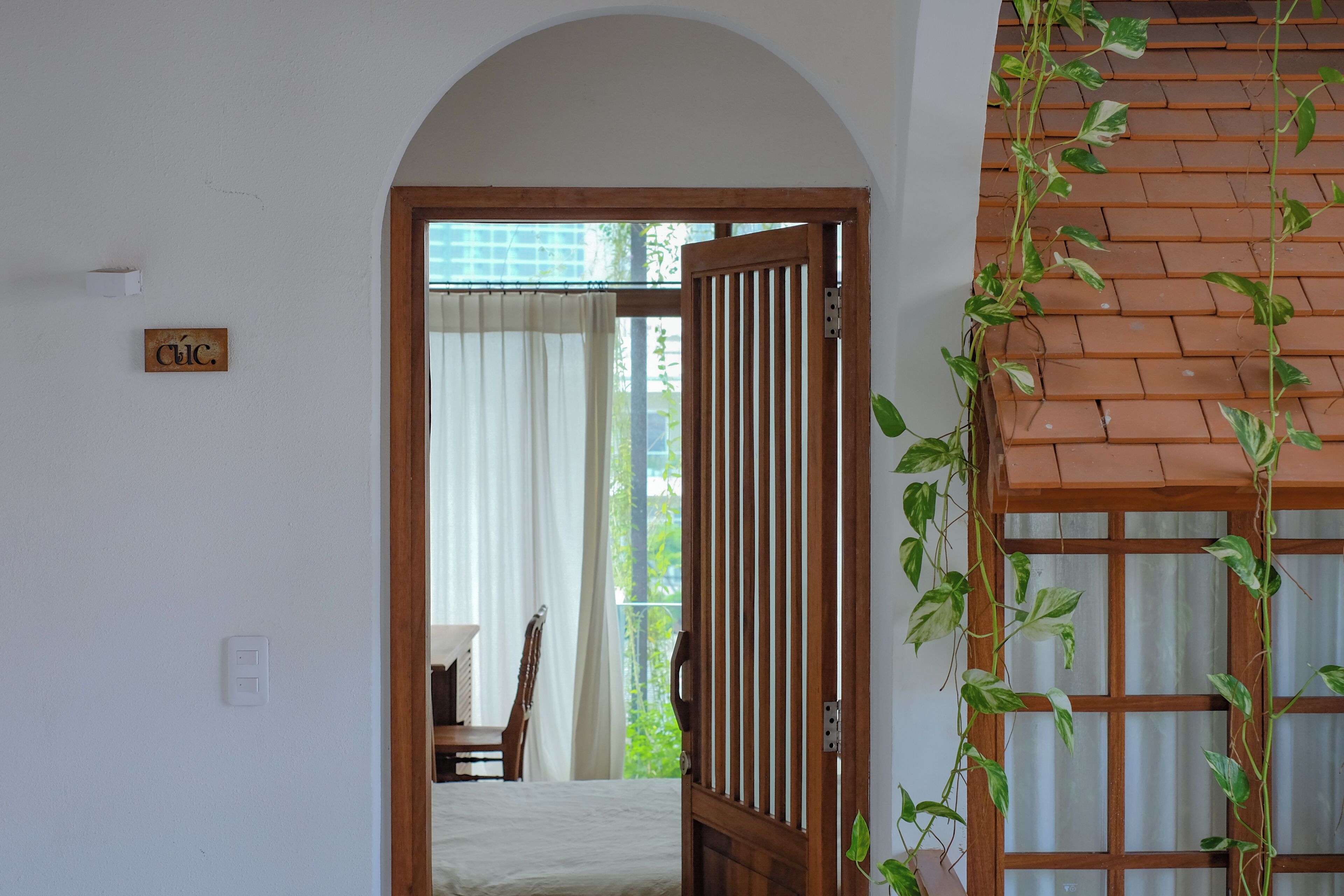 A doorway leading to a room with a bed, a chair, and a window with curtains.