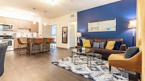 Un salon moderne avec un canapé en cuir marron, une table basse en verre et un mur d’accent bleu.