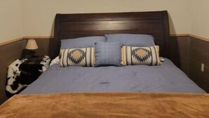 A bedroom with a single bed, a wooden headboard, a nightstand with a lamp, and patterned pillows. - Glacier Park <br>Rising Wolf Johnson Ranch RV and Cabins  (East Glacier Park)