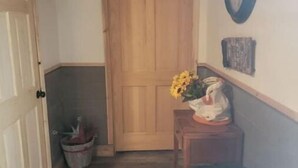 A hallway with a wooden door, a clock on the wall, a small table with a vase of flowers, and a trash bin. - Glacier Park <br>Rising Wolf Johnson Ranch RV and Cabins  (East Glacier Park)