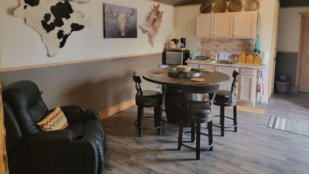 A modern living room with a black leather sofa, a round dining table with four chairs, and a ceiling fan. - Glacier Park <br>Rising Wolf Johnson Ranch RV and Cabins  (East Glacier Park)