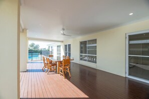 A spacious room with a wooden deck, a dining table with chairs, a ceiling fan, and large windows. - Parkside Getaway | Pool, Family Entertainer (Dubbo)