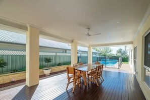 An outdoor patio with a wooden table and chairs, a pool, and a covered area with a ceiling fan. - Parkside Getaway | Pool, Family Entertainer (Dubbo)