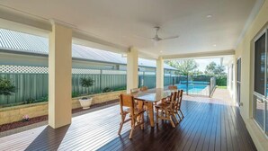 Une terrasse extérieure avec une table et des chaises en bois, un ventilateur de plafond et une vue sur une piscine.