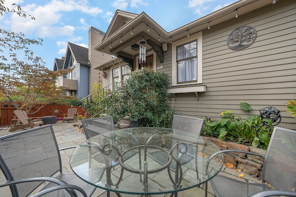 A glass-top table with metal chairs in a backyard with a house in the background.