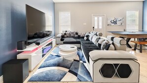 Een moderne woonkamer met een hoekbank, een flatscreen televisie, een tafeltennistafel en een plafondventilator.