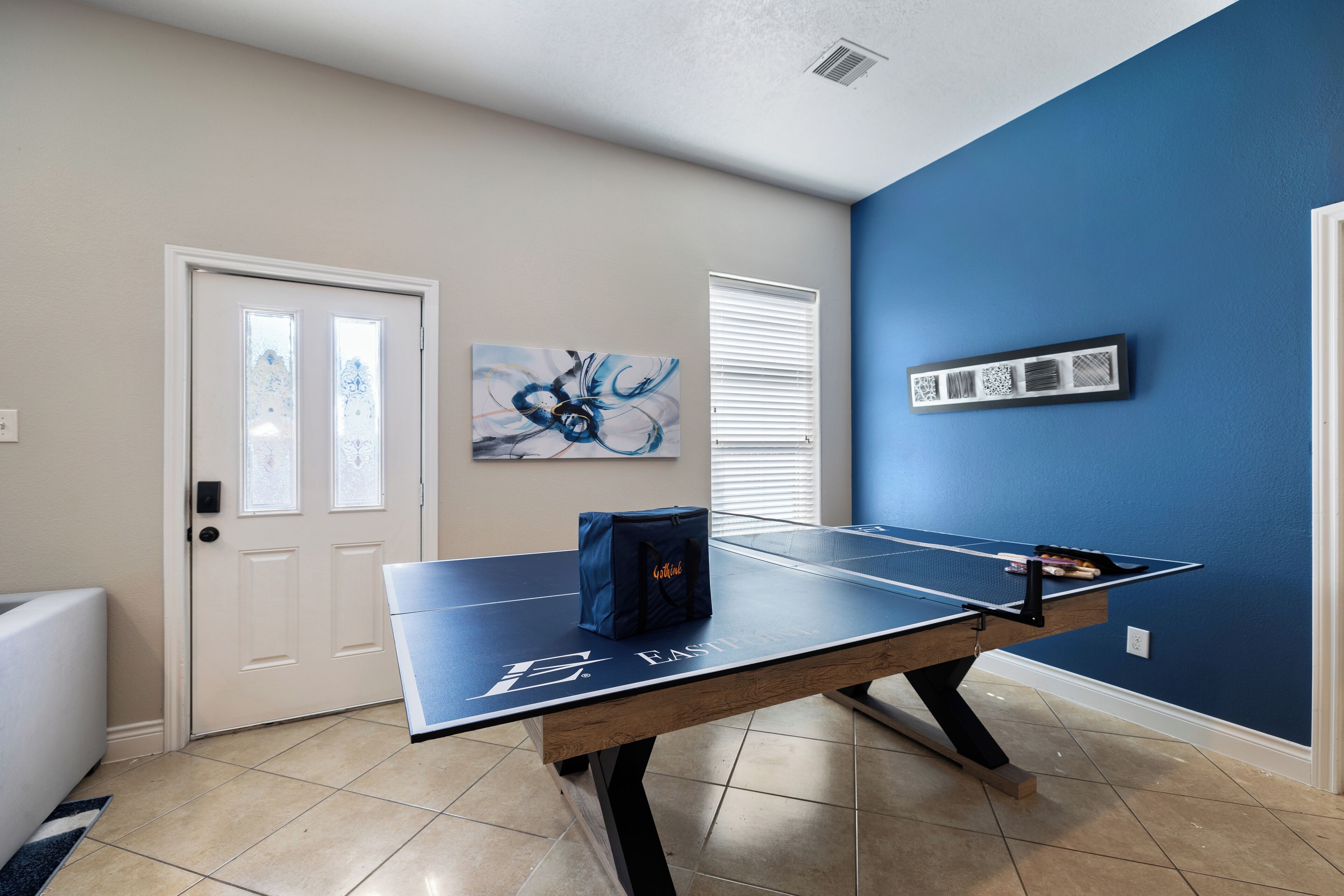 A ping pong table in a room with blue walls, a white door, and a painting on the wall.