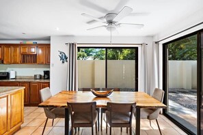 A dining area with a wooden table and chairs, a ceiling fan, and a view through large sliding glass doors.