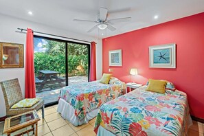 A room with two beds, a chair, a table, and a ceiling fan. - Inviting Home with Colorful Decor and Private Backyard Oasis with a Swimming Pool & Shaded Terrace (Santa Cruz)