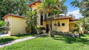 A two-story yellow building with a tiled roof, surrounded by lush greenery and palm trees. - Inviting Home with Colorful Decor and Private Backyard Oasis with a Swimming Pool & Shaded Terrace (Santa Cruz)