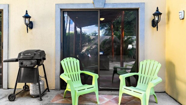 A patio area with a grill, two chairs, and a sliding glass door. - Inviting Home with Colorful Decor and Private Backyard Oasis with a Swimming Pool & Shaded Terrace (Santa Cruz)