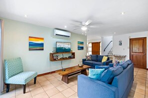 A living room with a sofa, a coffee table, a TV, and artwork on the walls. - Inviting Home with Colorful Decor and Private Backyard Oasis with a Swimming Pool & Shaded Terrace (Santa Cruz)