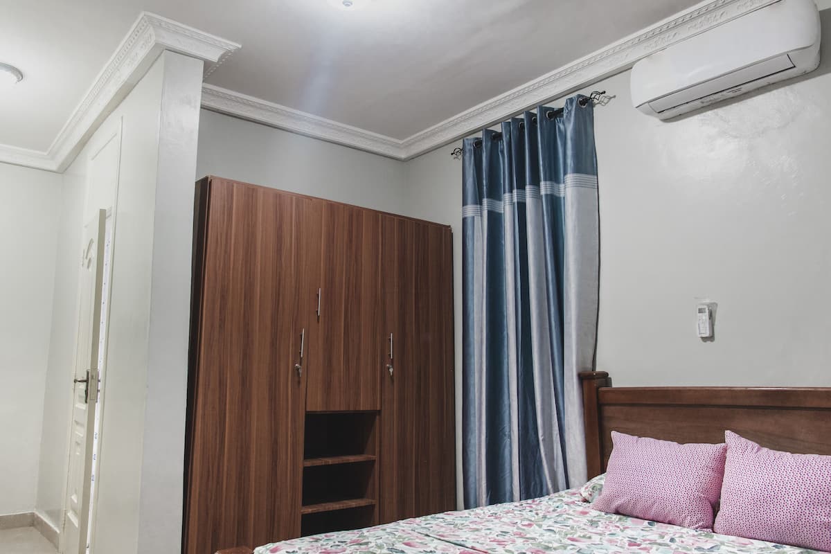 Une chambre avec une armoire en bois, un lit avec des coussins roses et un rideau bleu.