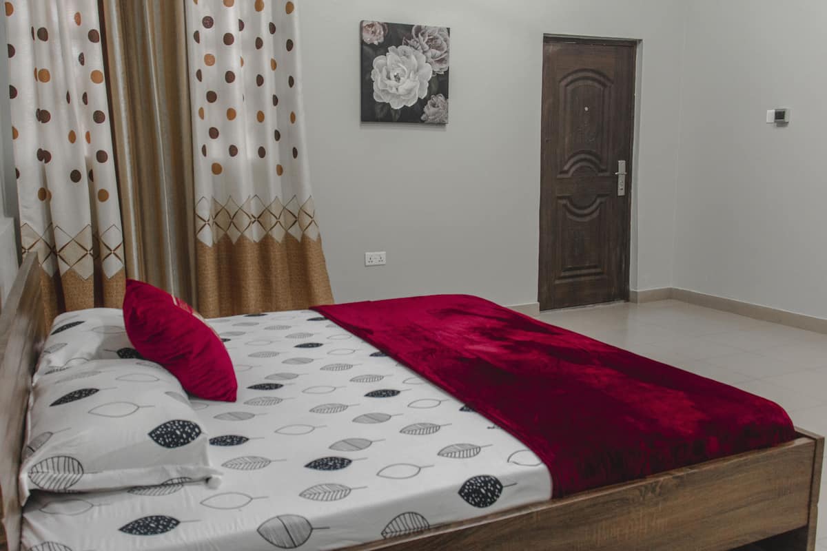 Une chambre à coucher avec un lit, des rideaux, une porte et un tableau accroché au mur.