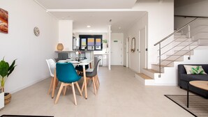 A modern living room with a sofa, a dining area with chairs and a table, and a staircase.