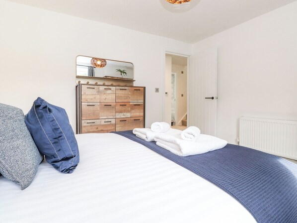 A bedroom with a bed, a wooden dresser, a mirror, and a door leading to another room.
