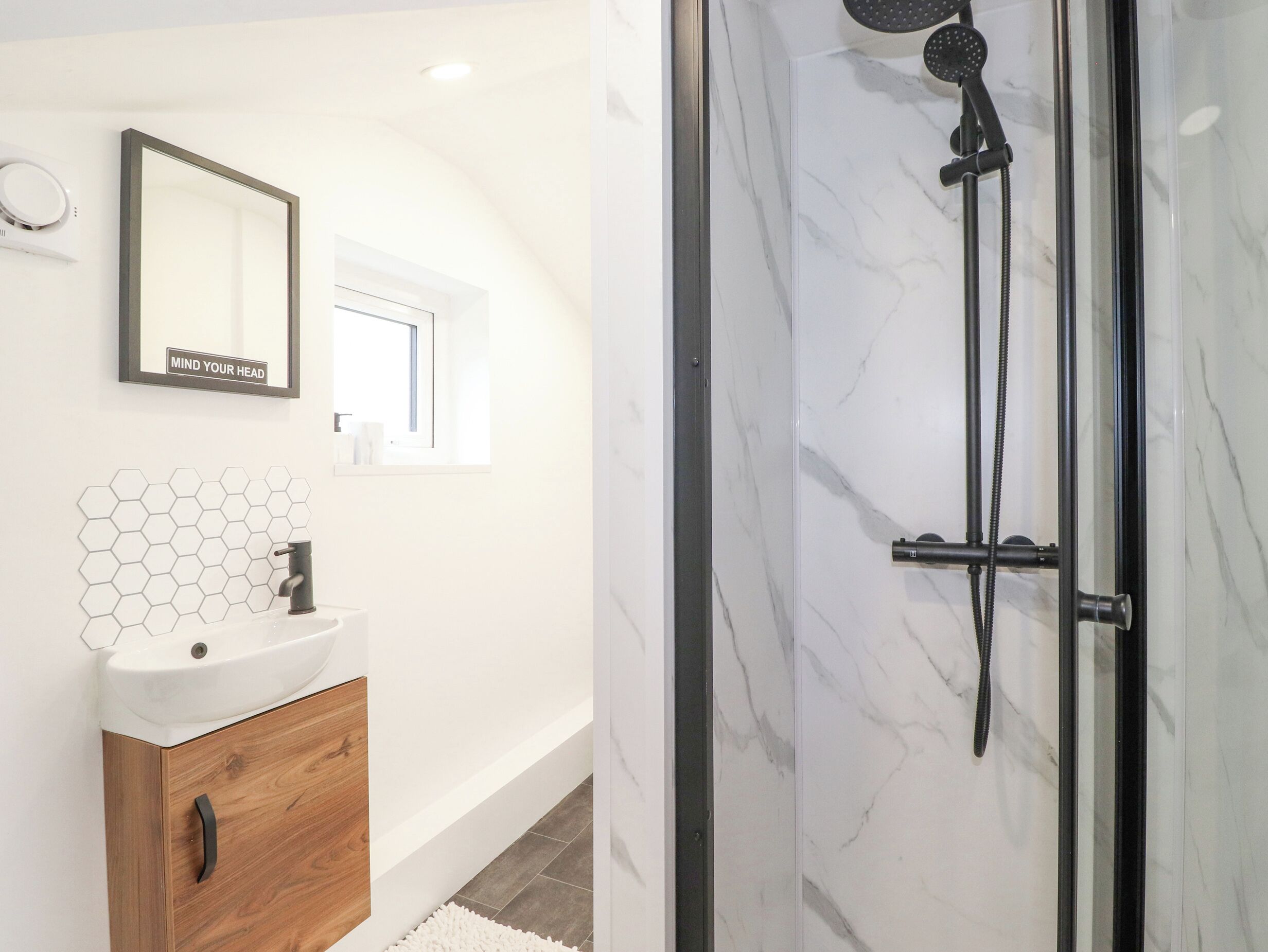Une salle de bain avec une douche en marbre, un meuble-lavabo en bois, un pare-chocs en carreaux hexagonaux et un miroir orné d'une citation inspirante.