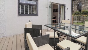 A patio with wicker furniture and a glass table, adjacent to a white building with a window and a door leading to an interior space. - Rydal Rock (Ambleside)