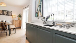 A modern kitchen with a large island, dark cabinetry, a sink with a black faucet, and a window with blinds. - Rydal Rock (Ambleside)