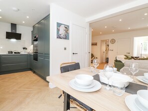 A modern kitchen with grey cabinets, a dining table set with white plates and glasses, and a living area with a sofa and a green chair. - Rydal Rock (Ambleside)