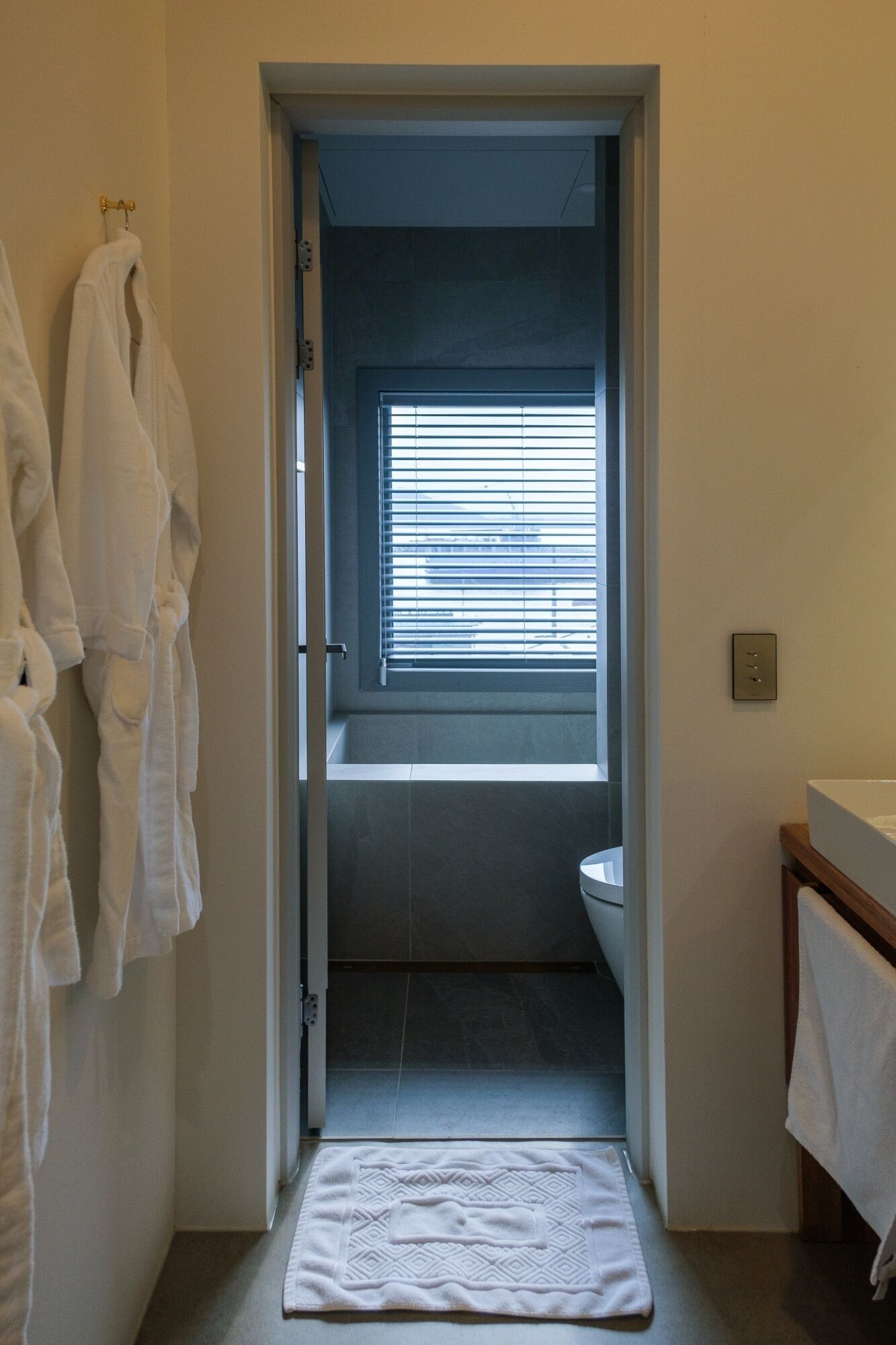 A bathroom with a bathtub, toilet, and a window with blinds. There are towels hanging on the wall.