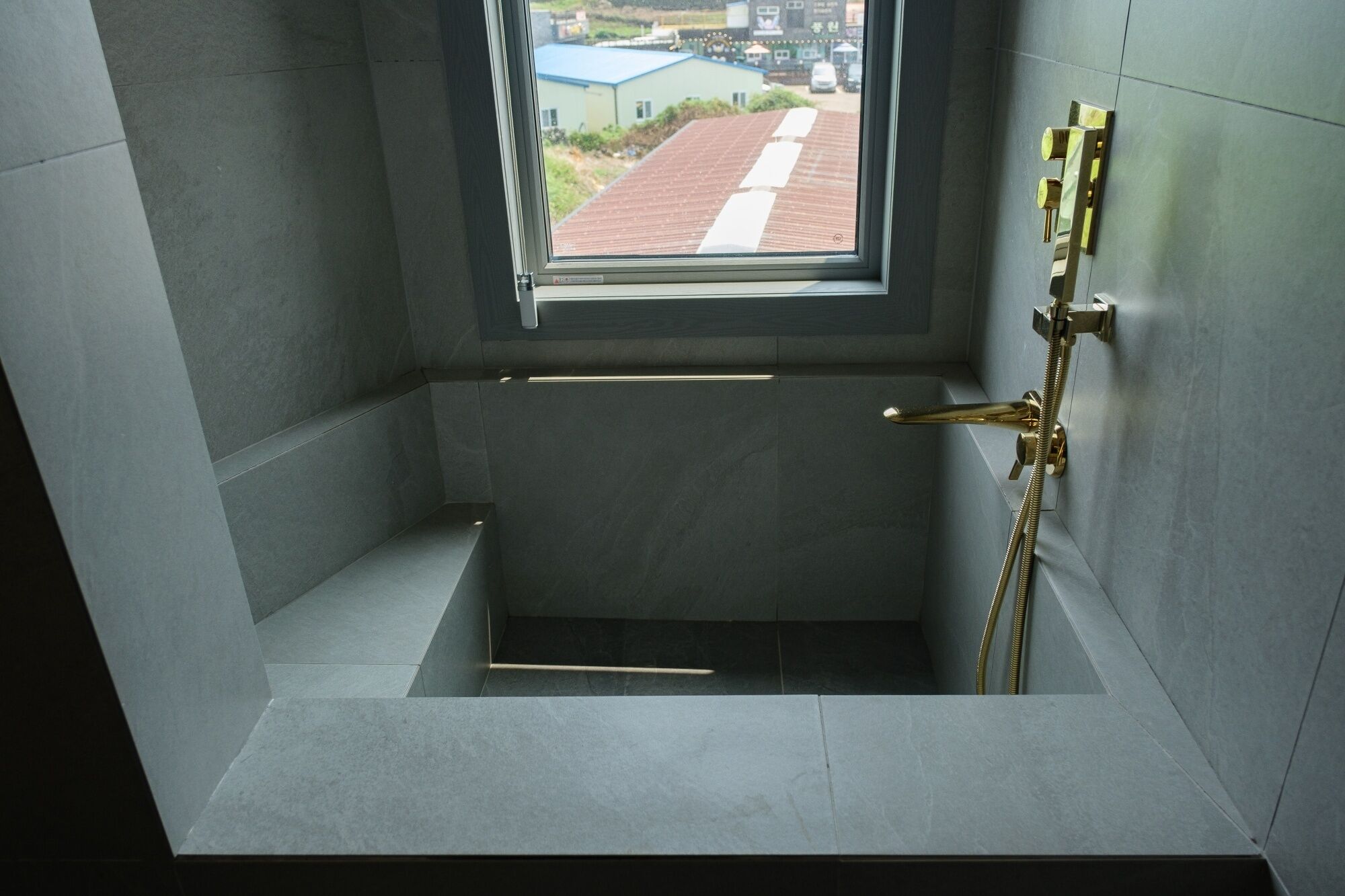 A modern bathroom with a built-in window, a shower, and a gold-colored faucet.