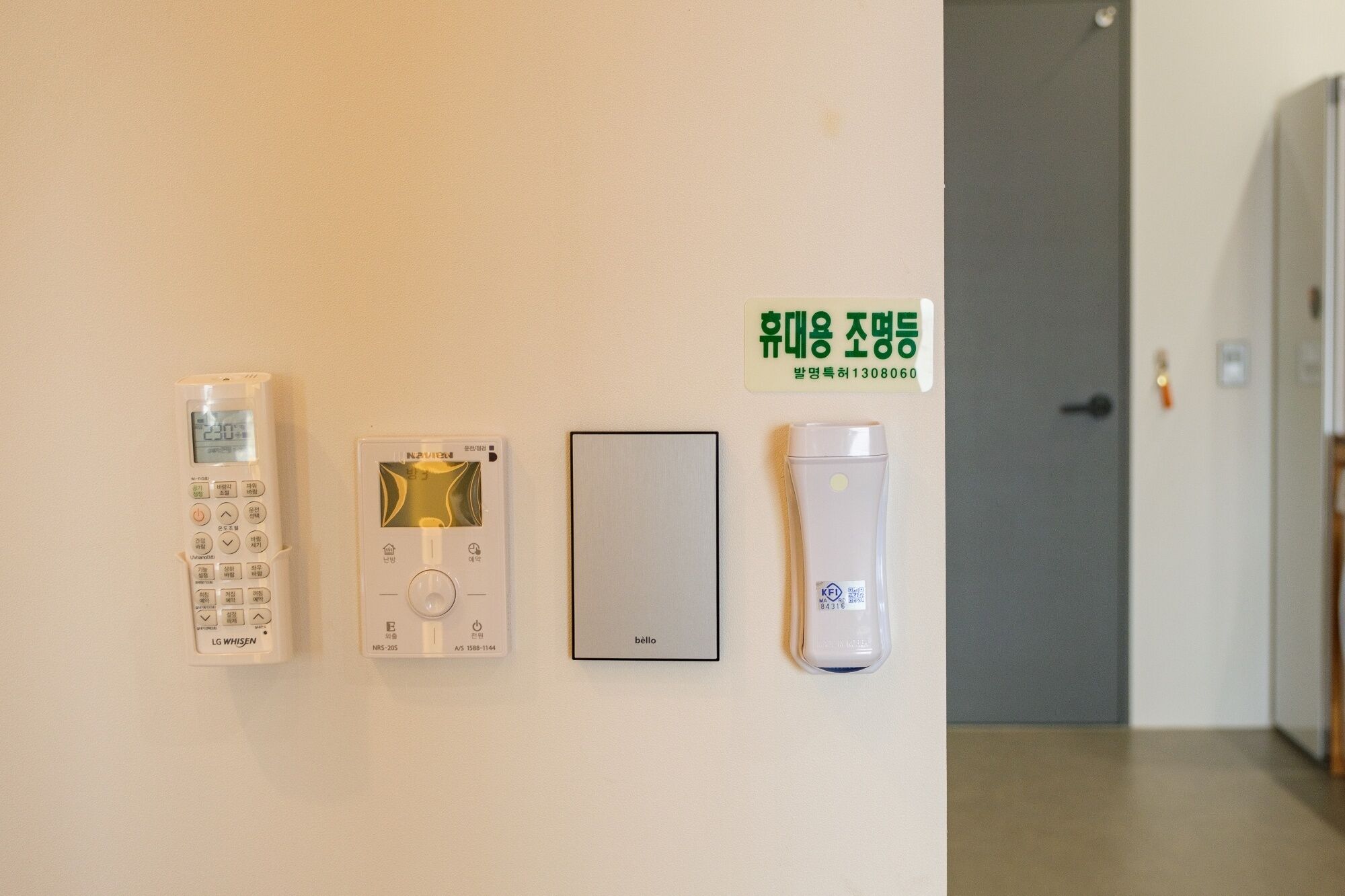 A wall-mounted control panel with a digital display, a thermostat, a light switch, and a smoke detector.