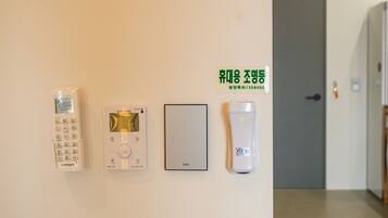 A wall-mounted control panel with a digital display, a thermostat, a light switch, and a smoke detector.