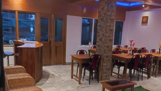 Un comedor con mesas y sillas de madera, una columna central y vistas al exterior a través de amplios ventanales.