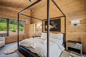 Une chambre à coucher dans un chalet en bois, avec un lit à baldaquin, un tableau représentant une tête de cerf et une vue sur la forêt.