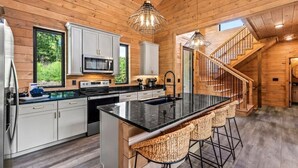 A modern kitchen with a central island, bar stools, a microwave, and a staircase leading to another level. - Starlight Ridge - Indoor pool & theater room (Smoky Mountains)