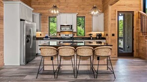A modern kitchen with wooden walls, a central island with bar stools, stainless steel appliances, and pendant lighting. - Starlight Ridge - Indoor pool & theater room (Smoky Mountains)